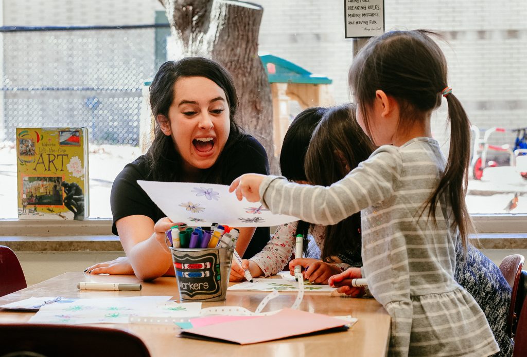 A woman smiles while working with preschool aged children in an early childhood education program.
