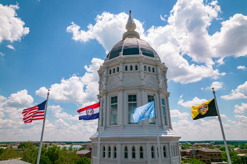 University of Missouri's Jesse Hall with the American flag, Missouri state flag, and the University of Missouri flag.
