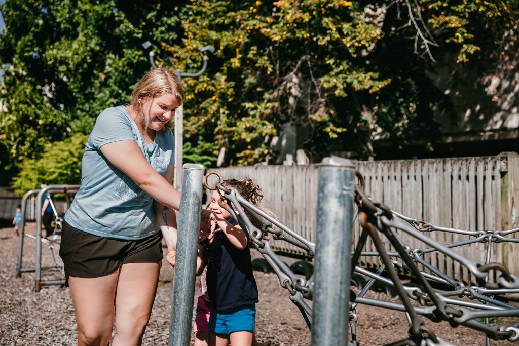 An early childhood professional plays with a young child on the playground.