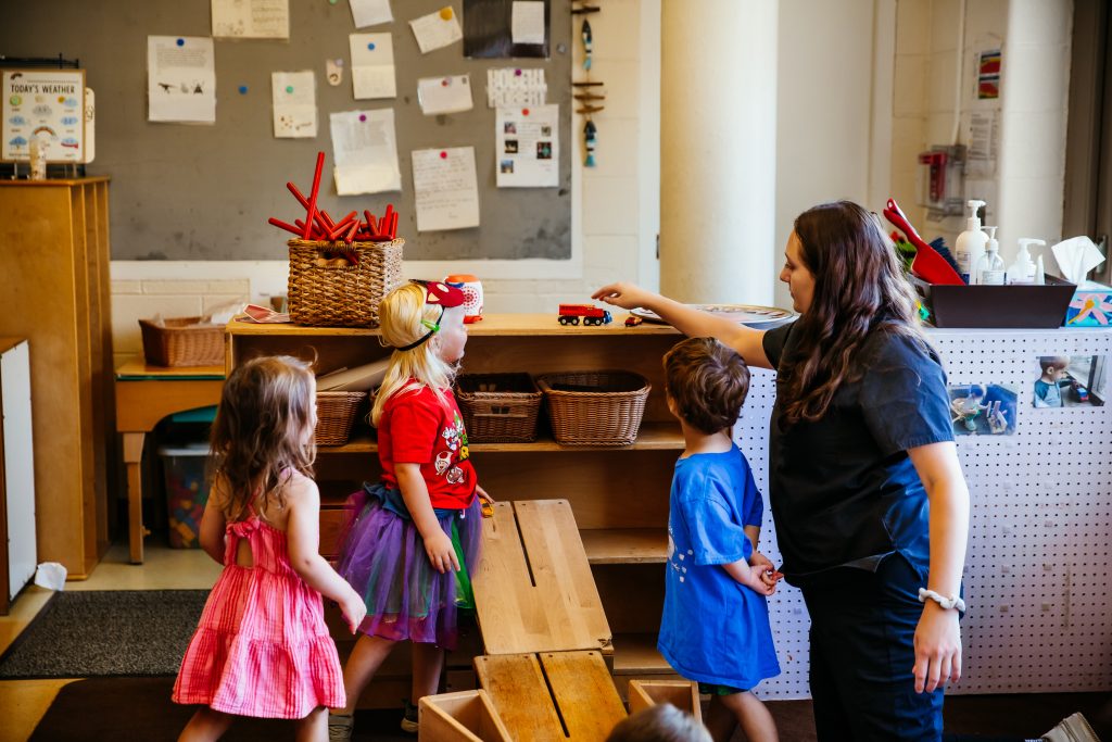An early childhood professional plays with preschool aged children at an early. childhood education program.