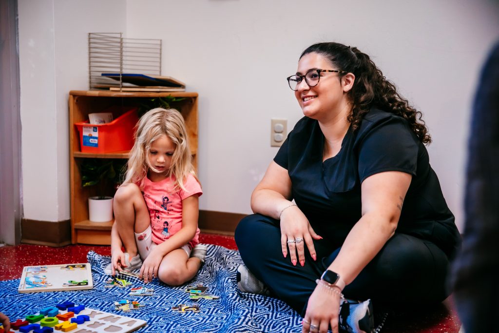 A woman sits with a preschool aged child in an early childhood education center.