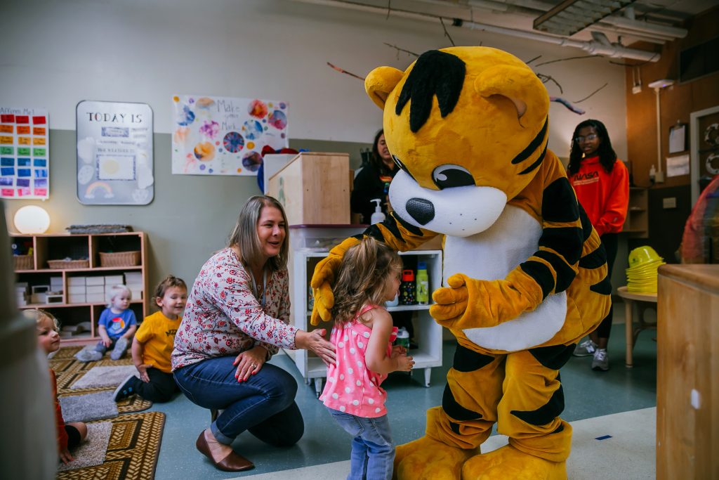 A woman smiles as a preschool aged child meets Mizzou's mascot Truman at an early childhood education program.