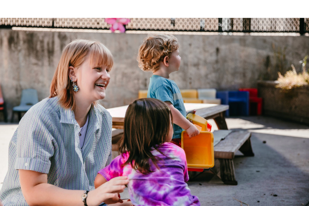 A woman smiles while working with young children.