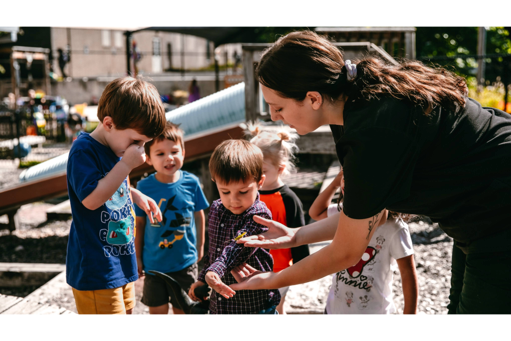 A teacher shows young children an insect on a child's sleeve.