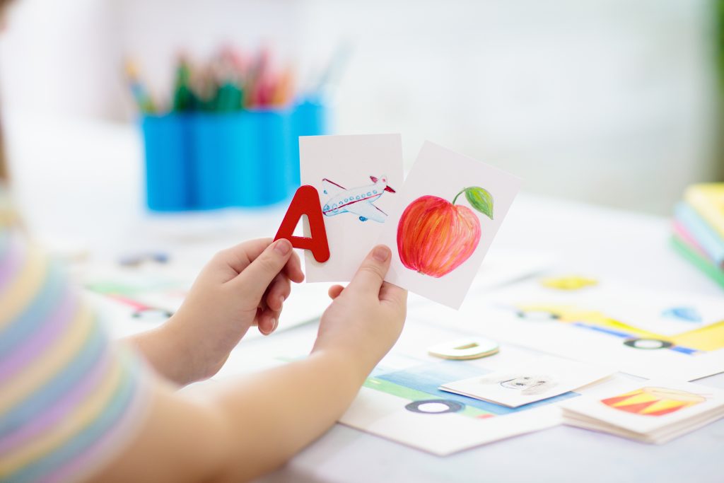 Young child's hands hold the letter A and a card with an airplane and another with an apple.